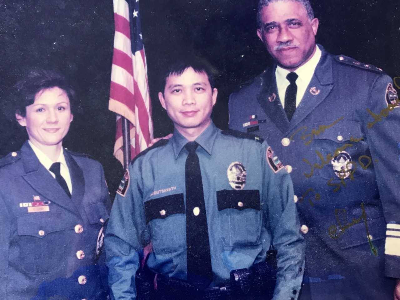 Ben Boutsavath in a police uniform, standing in front of an American flag with two other officers