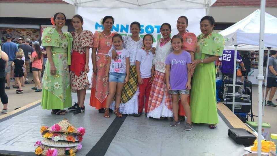 Group of women dressed in cultural clothing with a Minnesota State Fair banner in the background