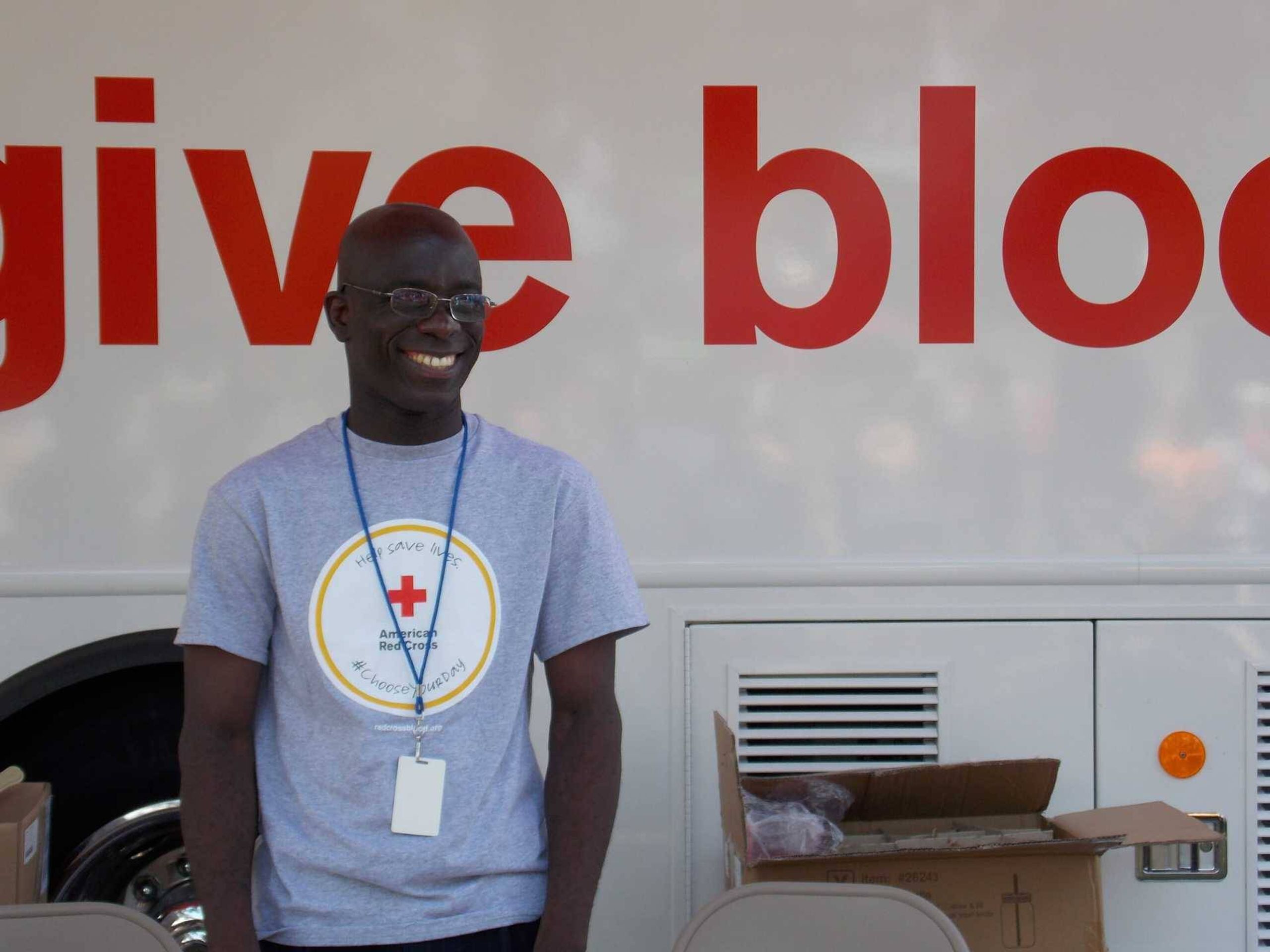 Man dressed in grey t-shirt standing outside of a van that reads "give blood"