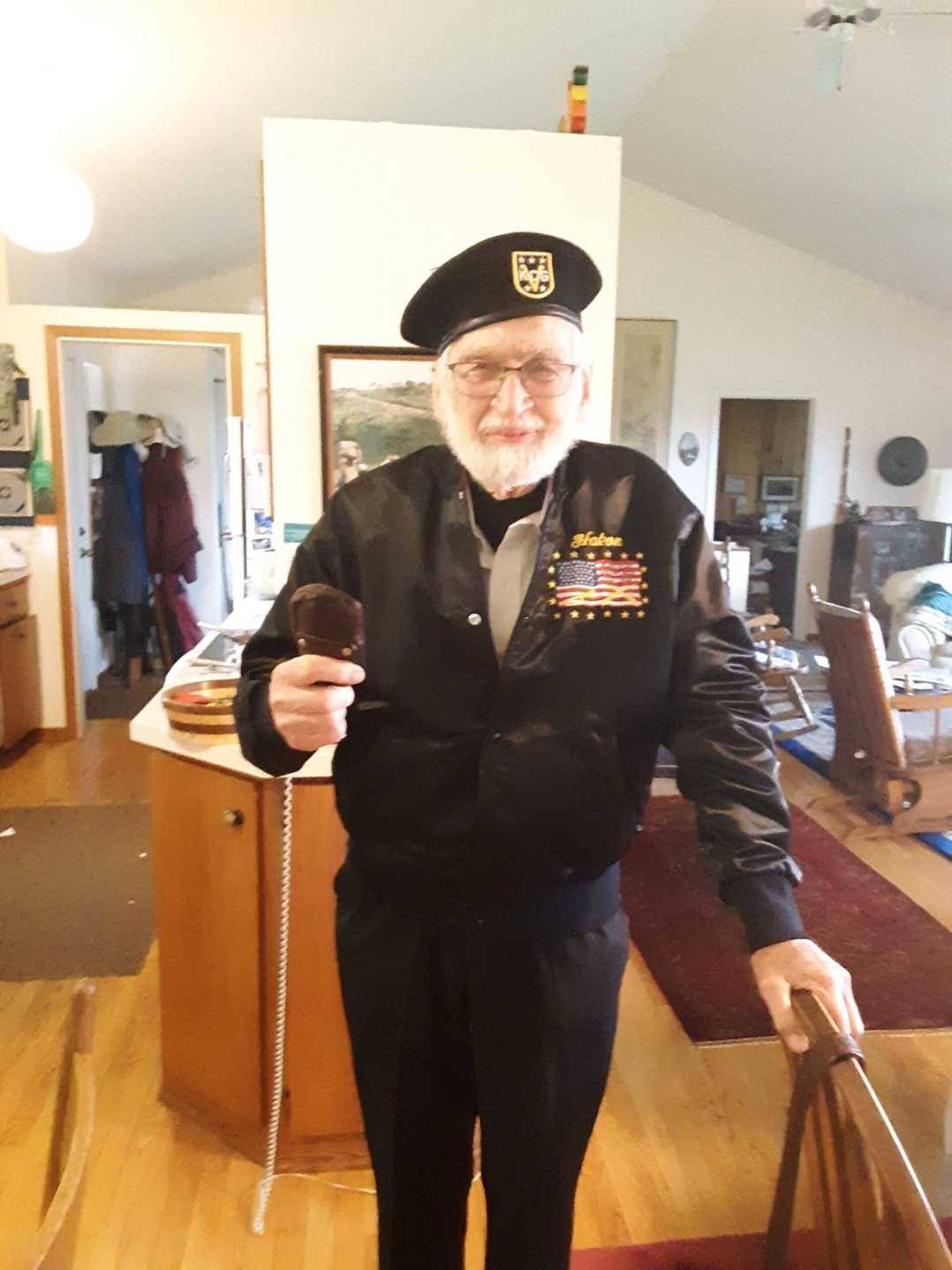 Man dressed in black uniform and black beret holding cane in living room