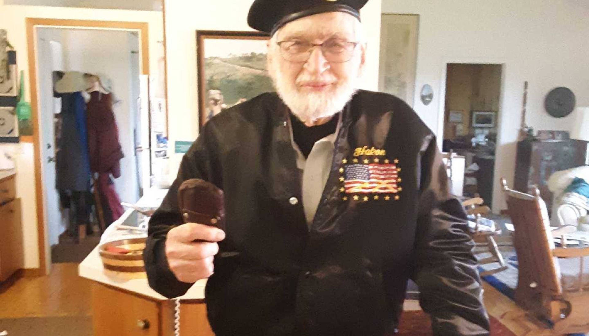 Man dressed in black uniform and black beret holding cane in living room