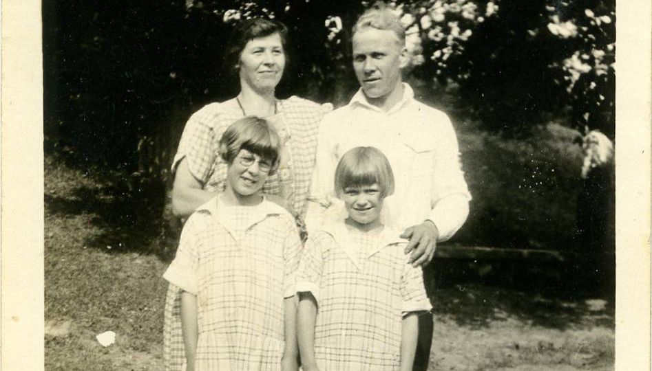 A man and woman and two girls dressed formally and standing in a field of grass