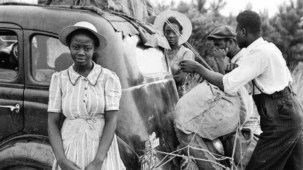 Family wearing 1940's era clothing strapping bags onto back of a car