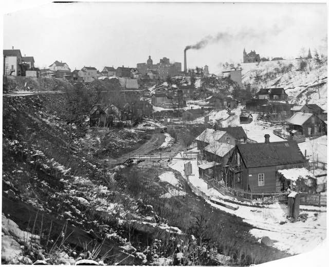 Black and white image of Swede Hollow homes with a smokestack in the distance