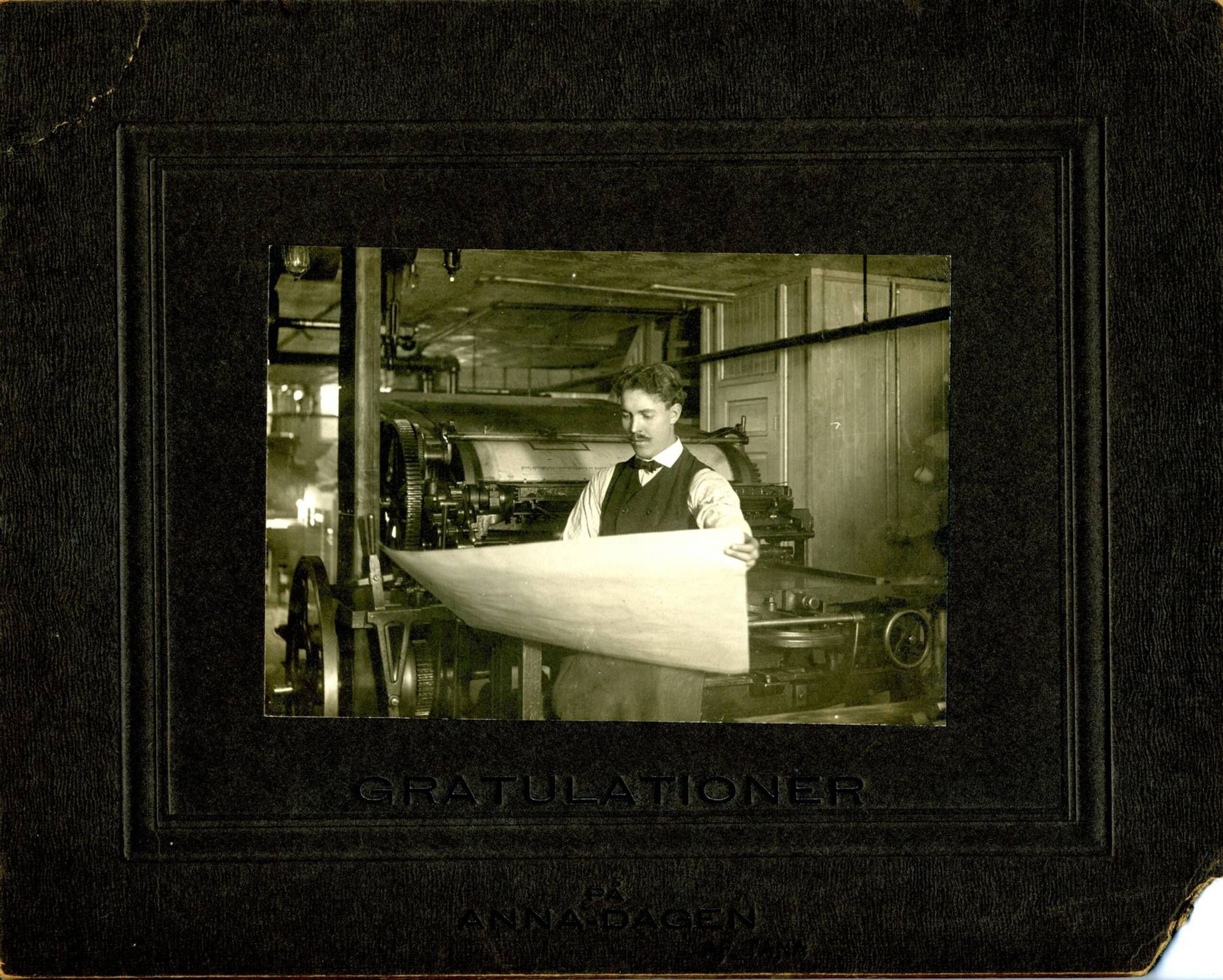 Man dressed formally standing in front of printing roll holding a piece of paper