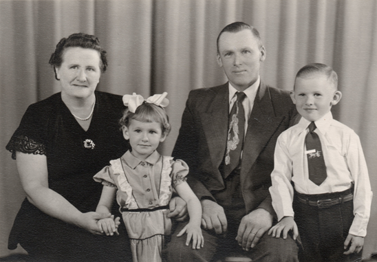 A man, woman, and two children dressed in formal clothes smiling