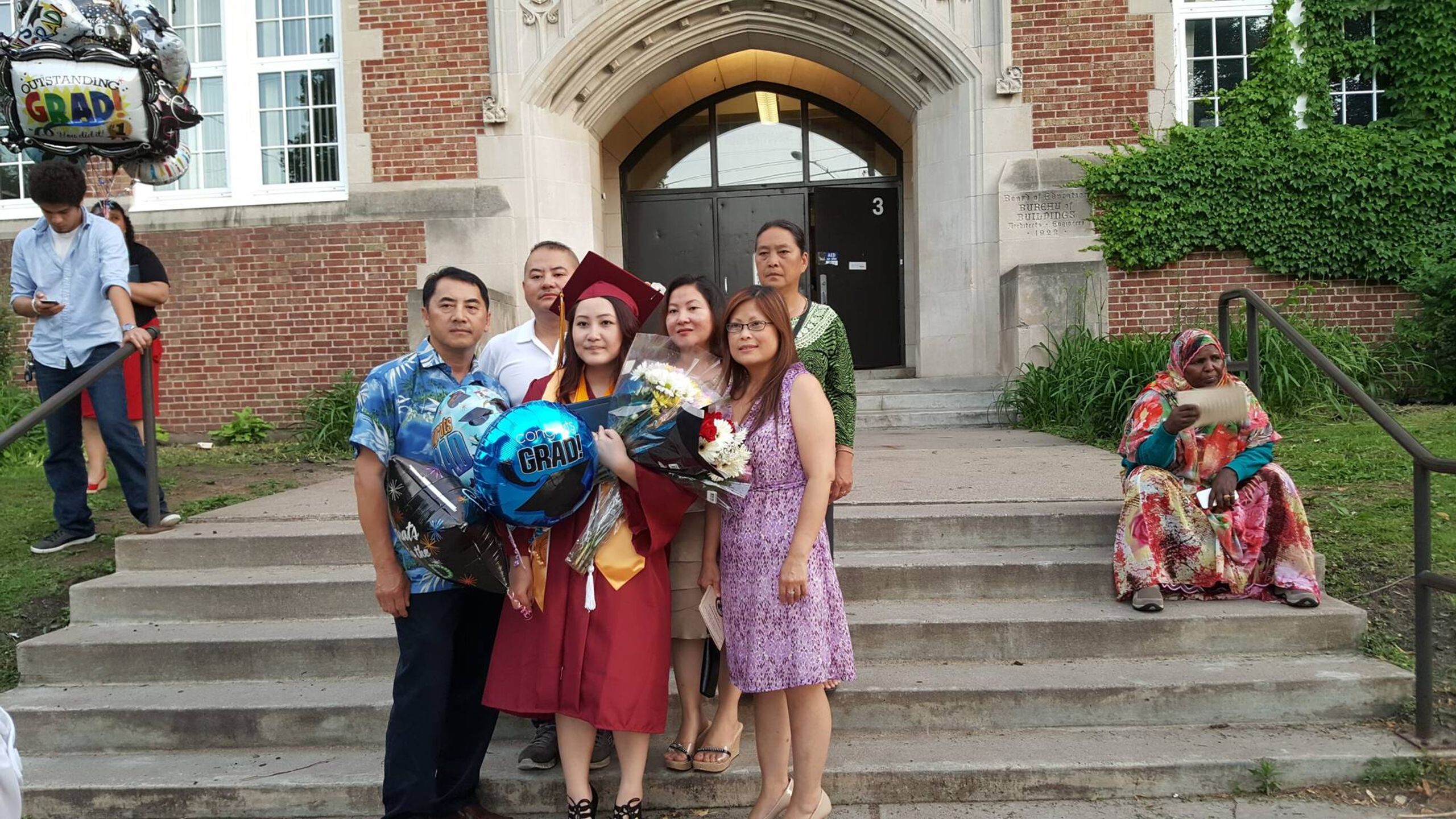 Family standing outside of a school hall with a college graduate