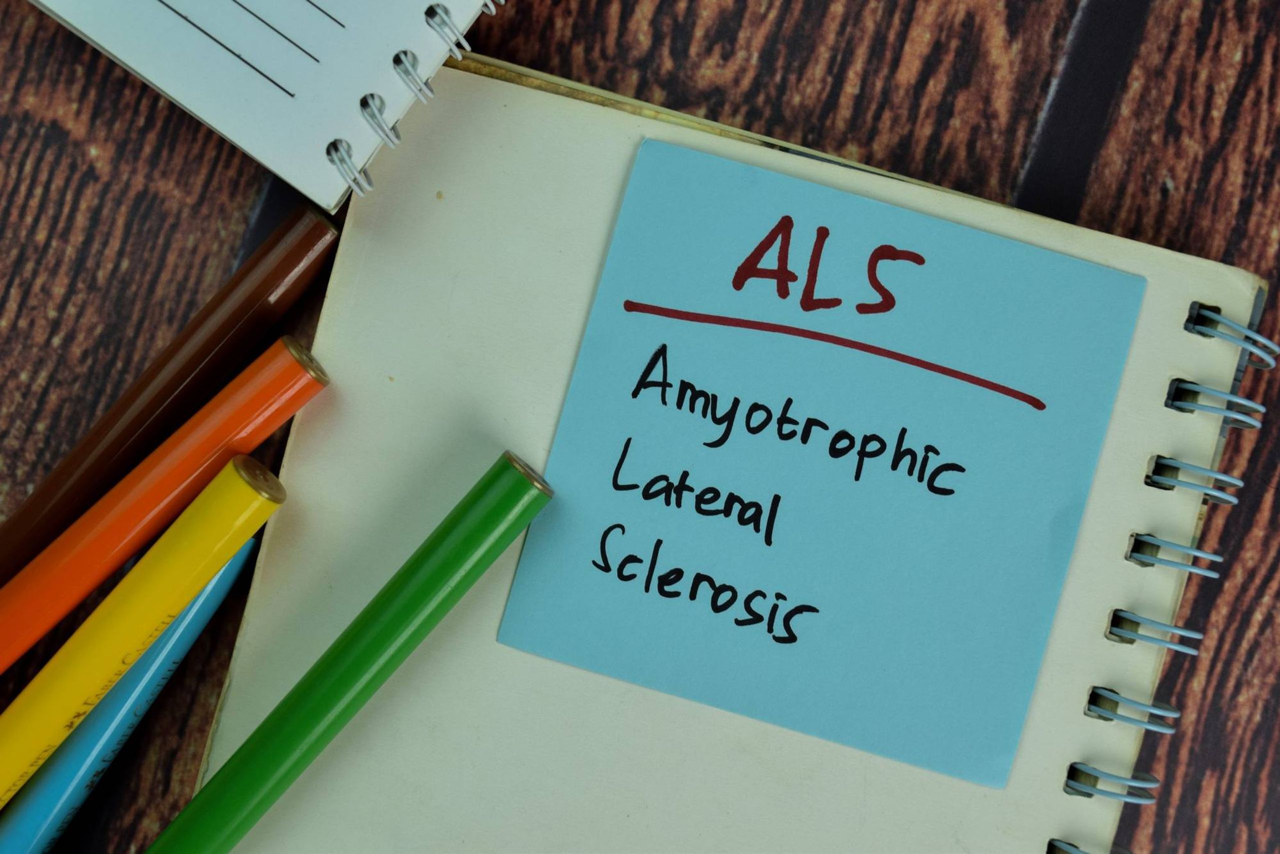 ALS - Amyotrophic Lateral Sclerosis write on sticky notes isolated on Wooden Table.