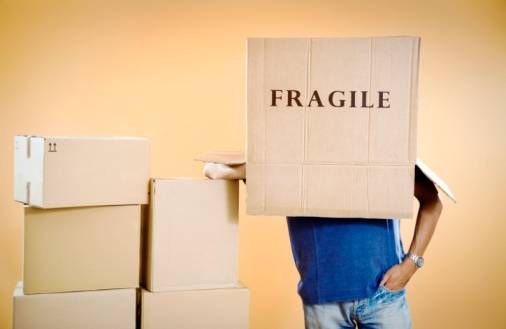 young adult with moving box on his head, fragile written on side