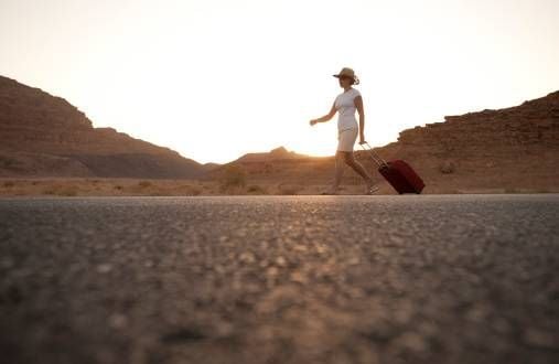 woman with a suitcase walking on road at sunset