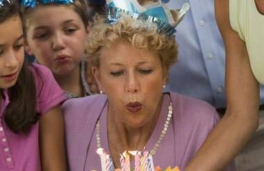senior woman blowing out candles on a birthday cake