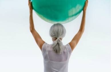 gray haired woman holding exercise ball over her head