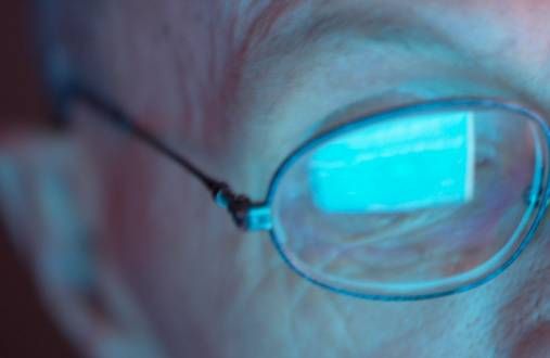 close up of man with glasses with computer glare reflected