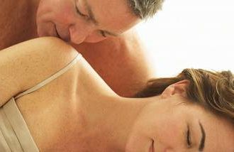 older man kissing woman's shoulder in bed