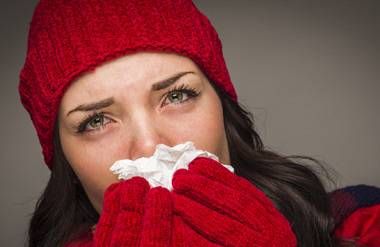 Woman with cold wearing hat and gloves and sneezing into kleenex