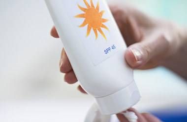 A woman squeezes sunscreen from a bottle