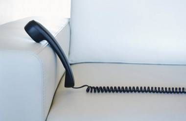 a black phone and its cord stretched on a white couch