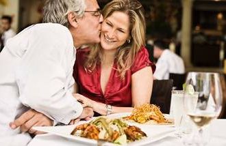 A mature man kissing his wife at a romantic dinner. 