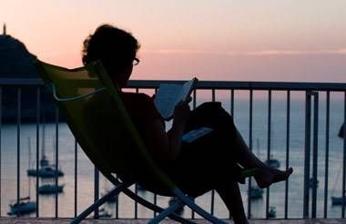 Woman sits near the beach, reading a book at sunset