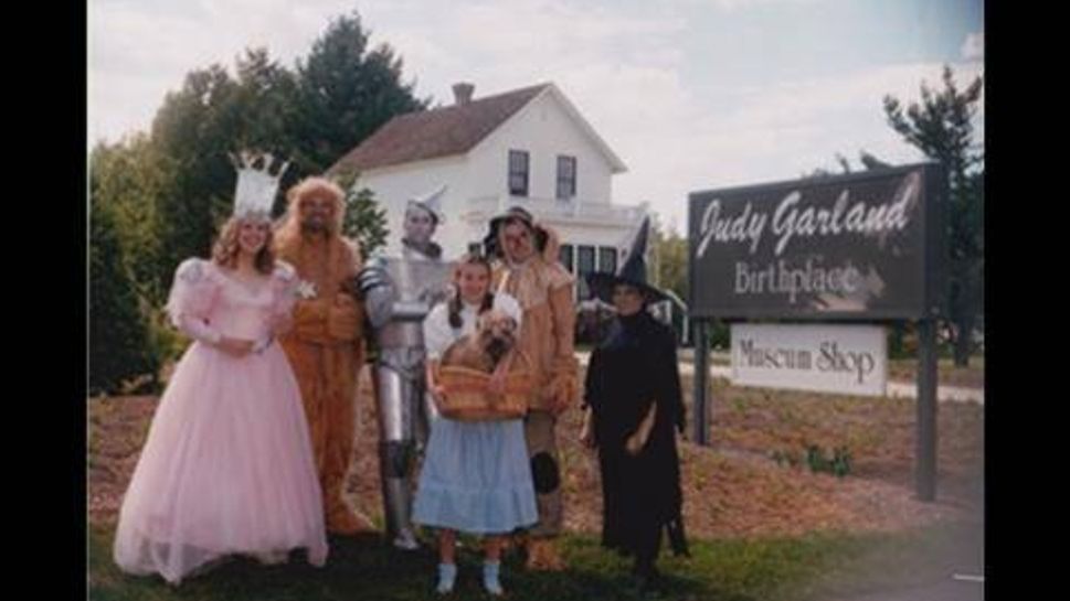 actors dress up as the wizard of oz characters in front of judy garland's house