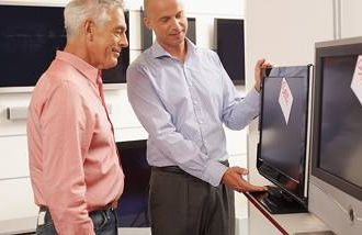 A man looking at flat screen TVs with a salesman.