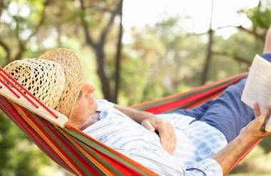 Mature man resting in a hammock, reading