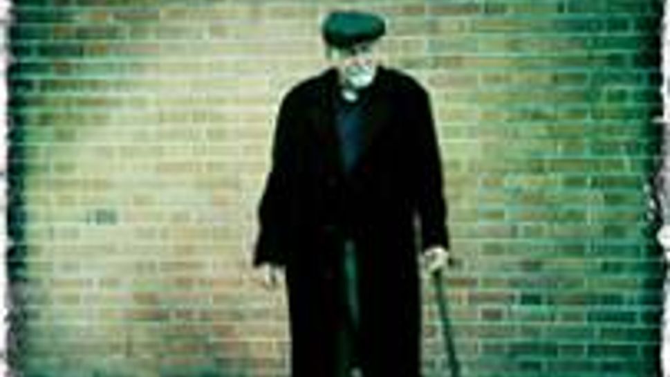 joe white standing outside in front of a brick wall wearing a black coat 