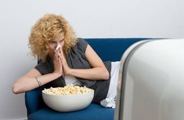 a woman blowing her nose in front of the TV with popcorn