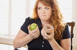 A woman holding an apple and a doughnut, knowing which is healthier to eat. 