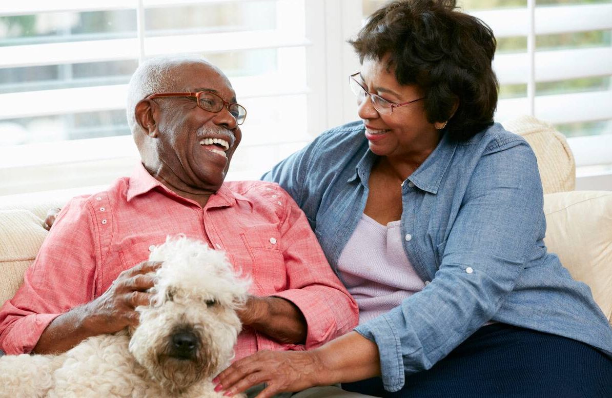 Happy Senior Couple Sitting On Sofa With Dog