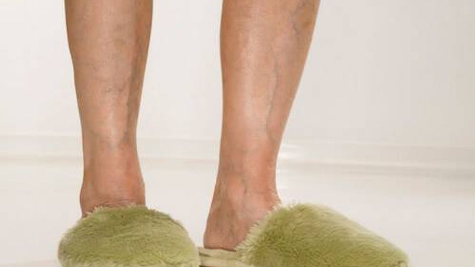 Caucasian senior female feet wearing green bedroom slippers.