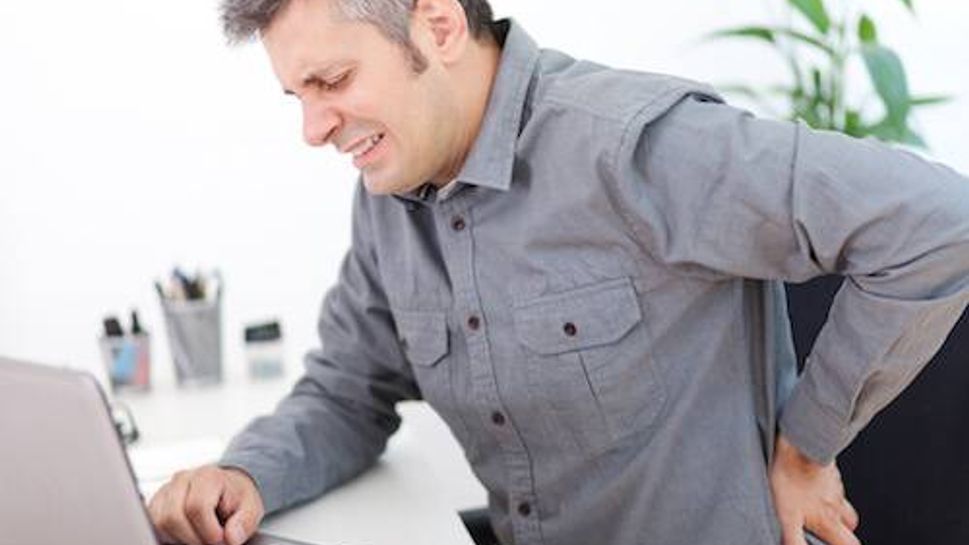 Image of a young man having a back pain while sitting at the working desk