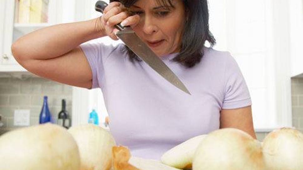 A woman wiping her tears while cutting onions