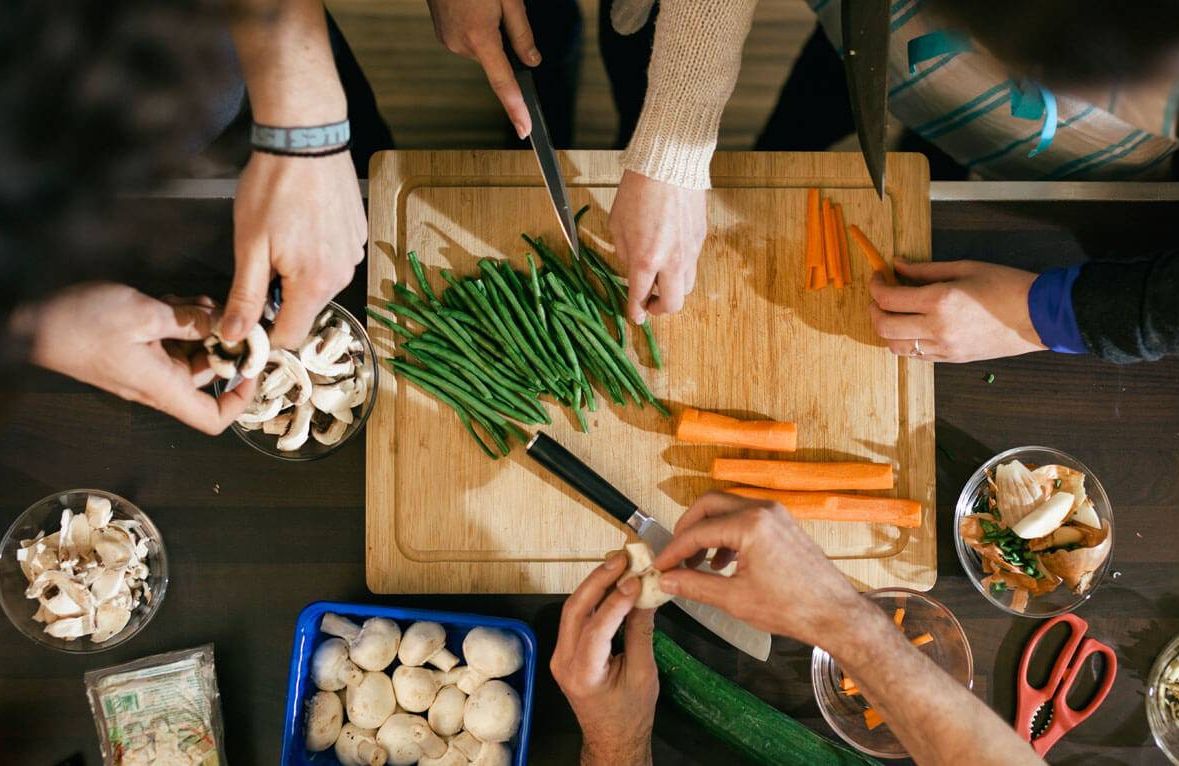 Close up of hands cutting vegetables on a wooden board in cooking class. Food like beans, carrots and mushrooms are getting ready to be cooked on a kitchen desk.