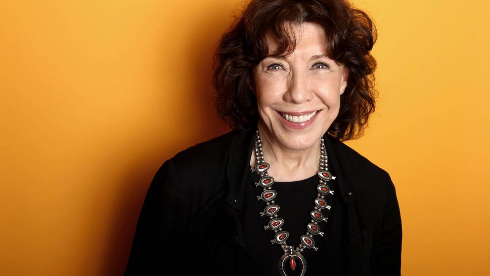 Actress Lily Tomlin standing against an orange background