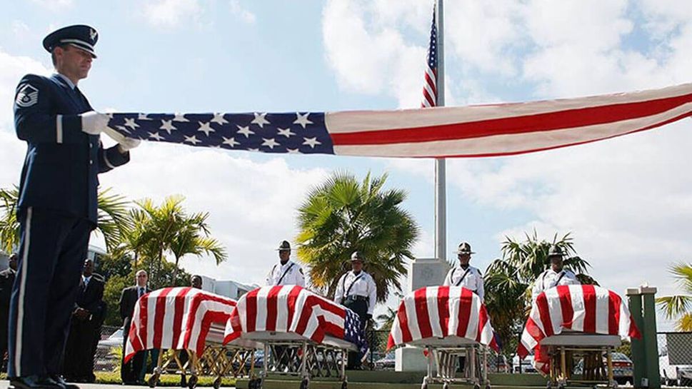 Master Sergeant, Francisco Navarro, from the Homestead Air Reserve folds an American flag in front of the four flag draped caskets holding the remains of four homeless United States military veterans.