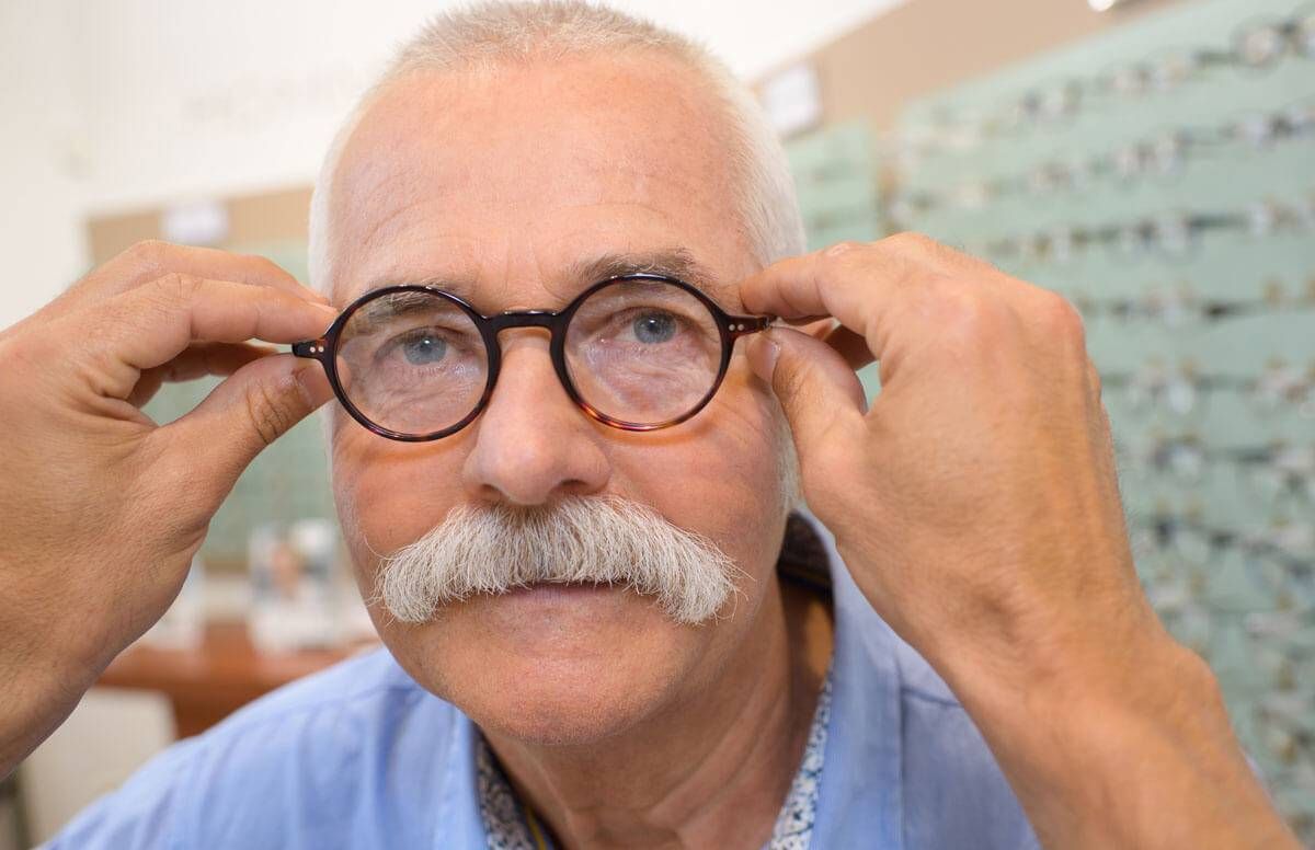 attractive senior man testing new glasses with optician
