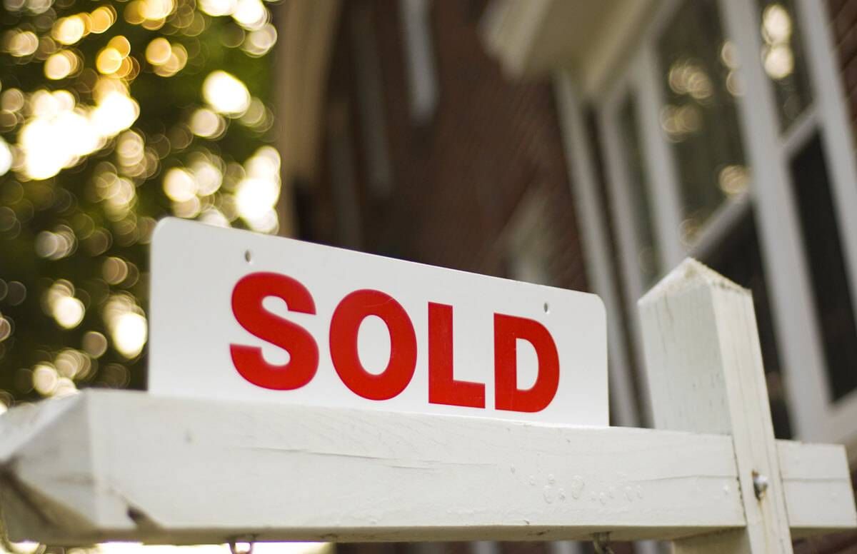 Real Estate "sold" sign with red brick building and trees blurry in the background