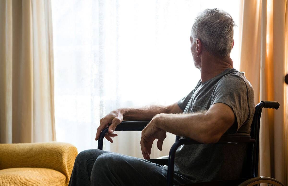 man sitting in wheel chair, looking out a window