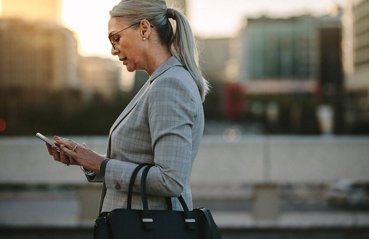 Professional business woman using mobile phone outdoors. Female texting on smart phone while walking outdoor in city.