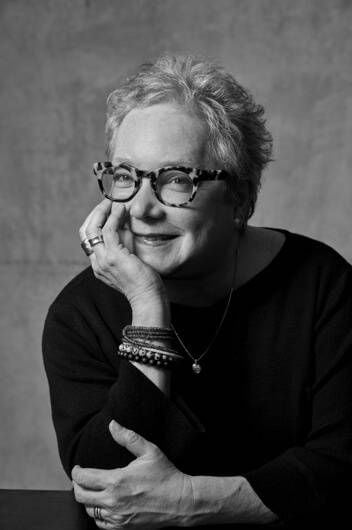 black and white headshot of woman with glasses and short hair leaning on a table with hand on chin