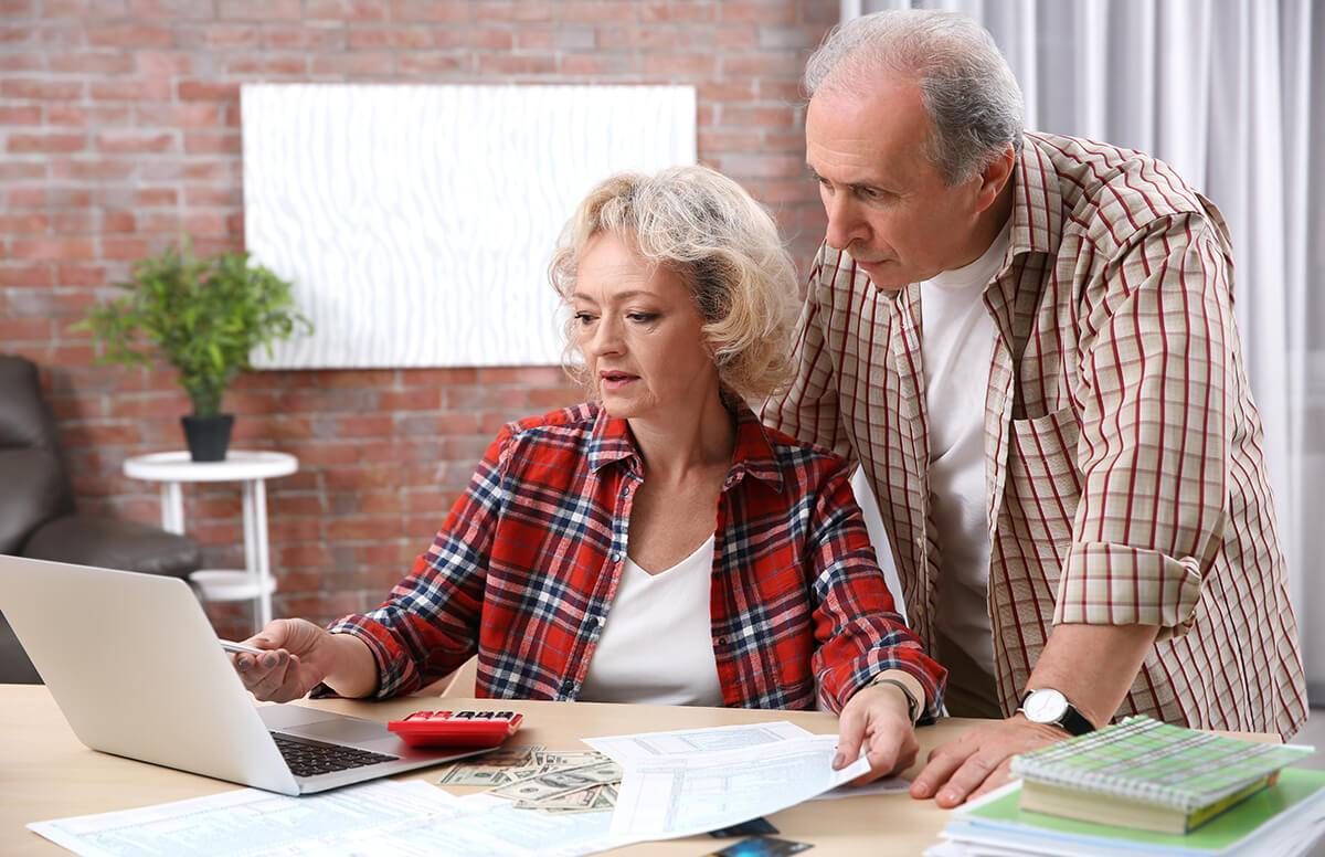 man and woman look at laptop together with papers, money, and calculator in front of them