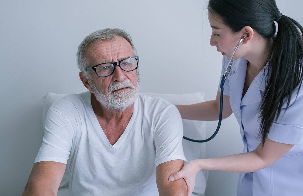 older man is examined by medical professional with a stethoscope