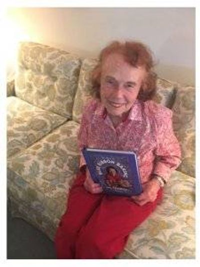 Marjorie Johnson sitting on her couch, holding a copy of her book