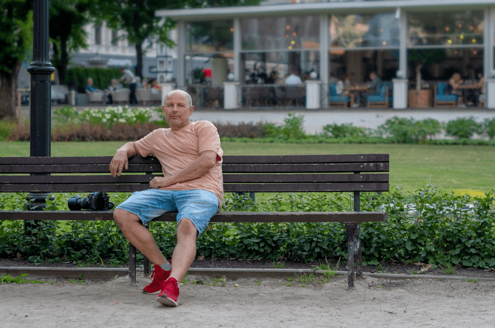 gentleman sitting on a bench in a park with a salmon shirt and shorts