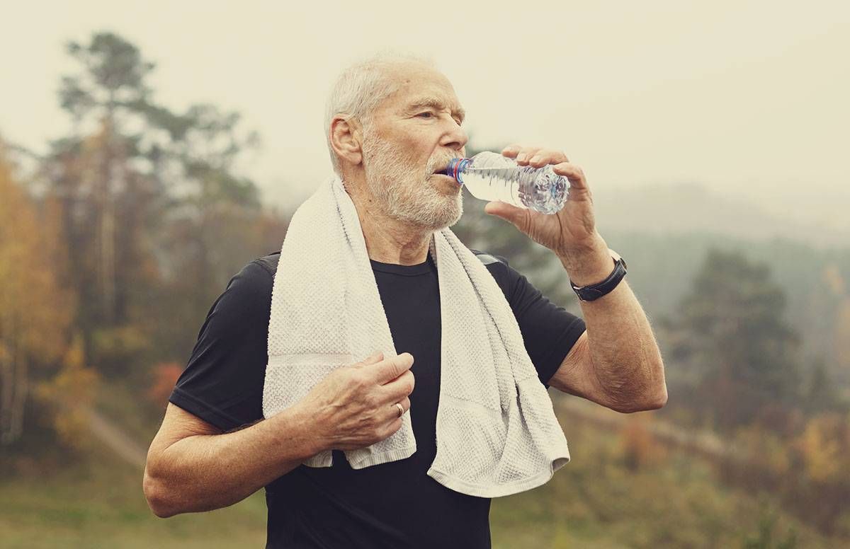 An older man stops to catch his breath and drunk water during an outdoor workout