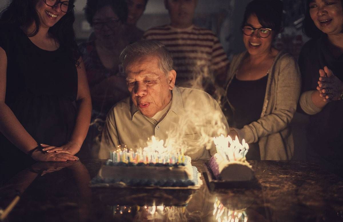 older man celebrating his birthday about to blow out candles on his birthday cake