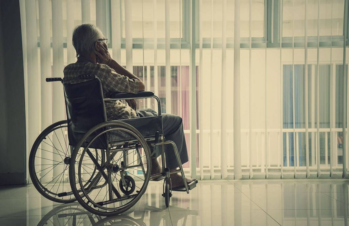 older man in a wheelchair, looking out a window