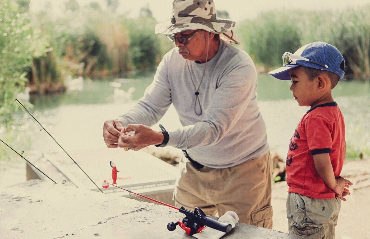 a grandfather helps his grandson bait a hook while they are fishing together