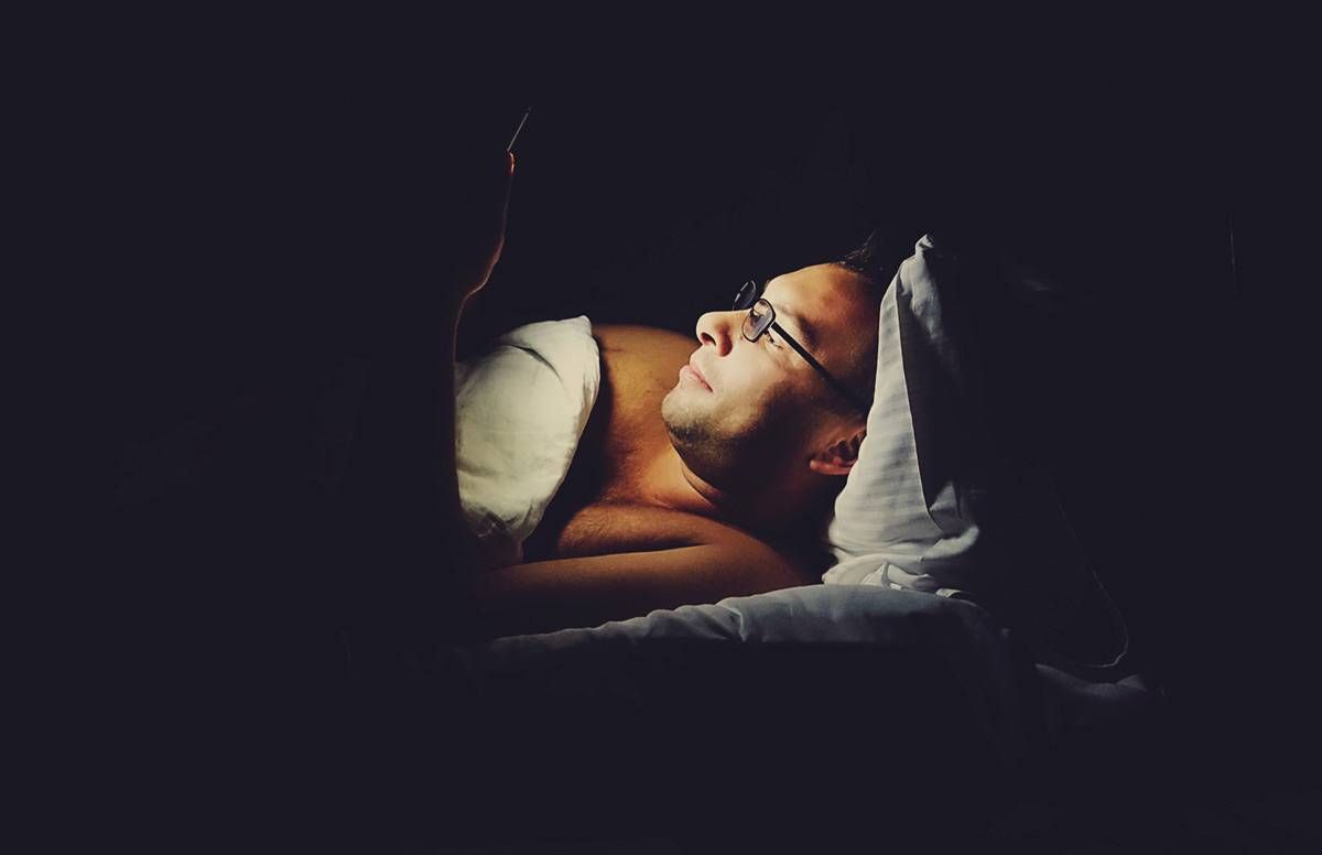 a man laying awake looking at his smartphone during the night